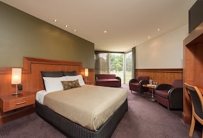 Quarto de hotel com uma cama grande, mesa de cabeceira, escrivaninha com cadeira, pequena mesa com cadeira e televisão fixada na parede.