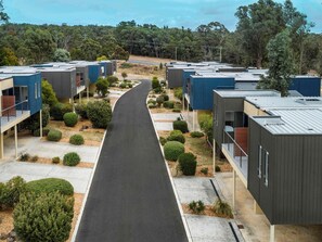 Una zona residencial moderna con casas compactas, un paseo central pavimentado y un fondo de árboles.