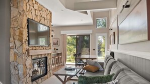 A modern living room with a stone fireplace, a flat-screen TV, a sofa, and a dining area with a table and chairs. - The Sebel Creswick Forest Resort (Creswick)