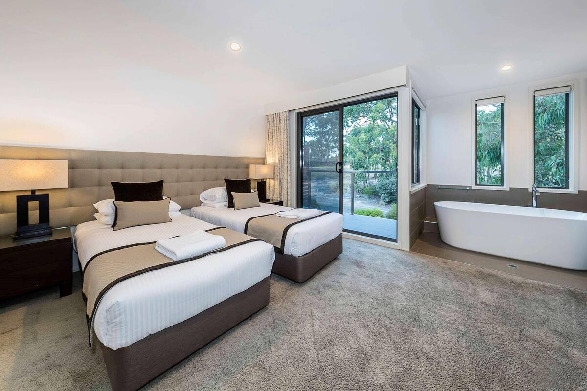 A hotel room with two beds, a large window, a bathtub, and a balcony.