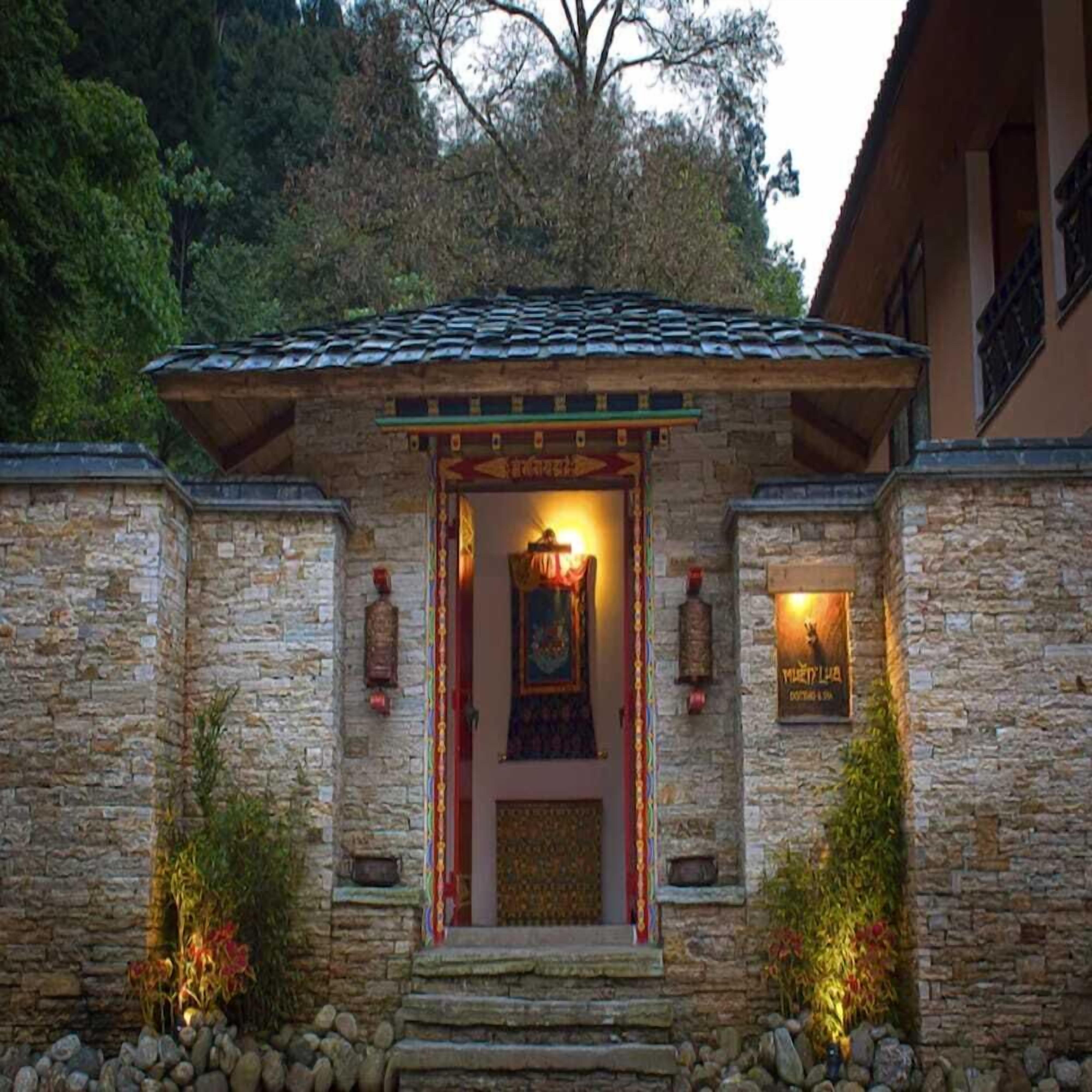 A stone building with a tiled roof, a central entrance with a framed artwork, and two lanterns on either side.