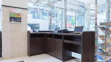 A reception area with a glass partition, a desk with a phone and laptop, and a magazine rack.