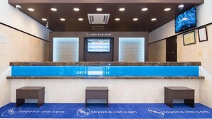 Un espace d’accueil avec un tapis bleu, un comptoir de réception et un écran numérique au-dessus.