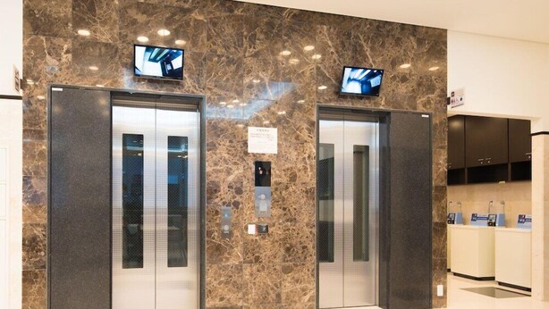 Un espace moderne pour les ascenseurs, avec des murs en marbre, deux ascenseurs et des écrans numériques au-dessus de chaque porte.