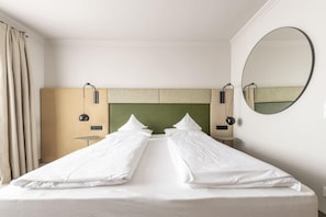 Una habitación de hotel con una cama, un espejo redondo, un cabecero y una mesita.