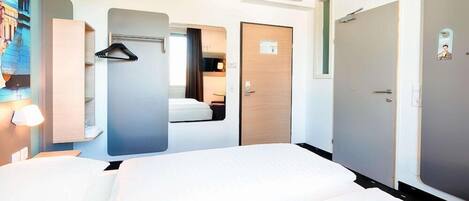 A hotel room with a bed, a wardrobe, a mirror, and a wall-mounted air conditioning unit.