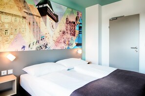 Una habitación de hotel con una cama, una mesita de noche, una lámpara de pared y una puerta.