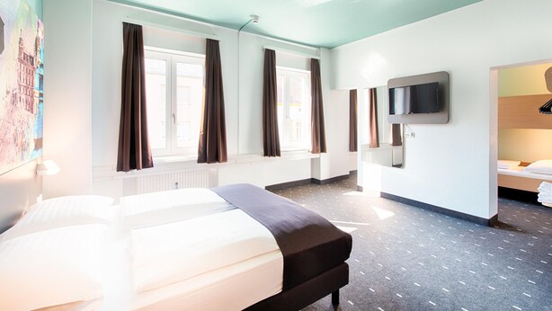 A hotel room with a bed, a TV mounted on the wall, and a window with curtains. - B B Hotel Graz Hbf (Graz)