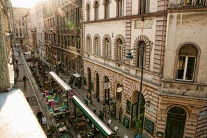 A street view of a historic building with a cafe on the ground floor, outdoor seating, and a tram line. - Palace Apartments (Budapest)