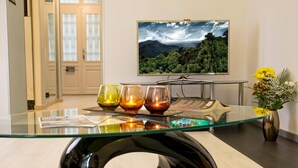 Un salon moderne avec une table basse en verre, un téléviseur à écran plat fixé au mur et un vase rempli de fleurs.