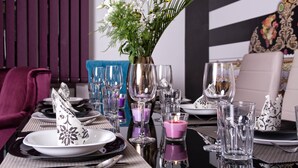 Une table à manger dressée avec des assiettes, des couverts et des verres, un vase rempli de fleurs et une bougie.