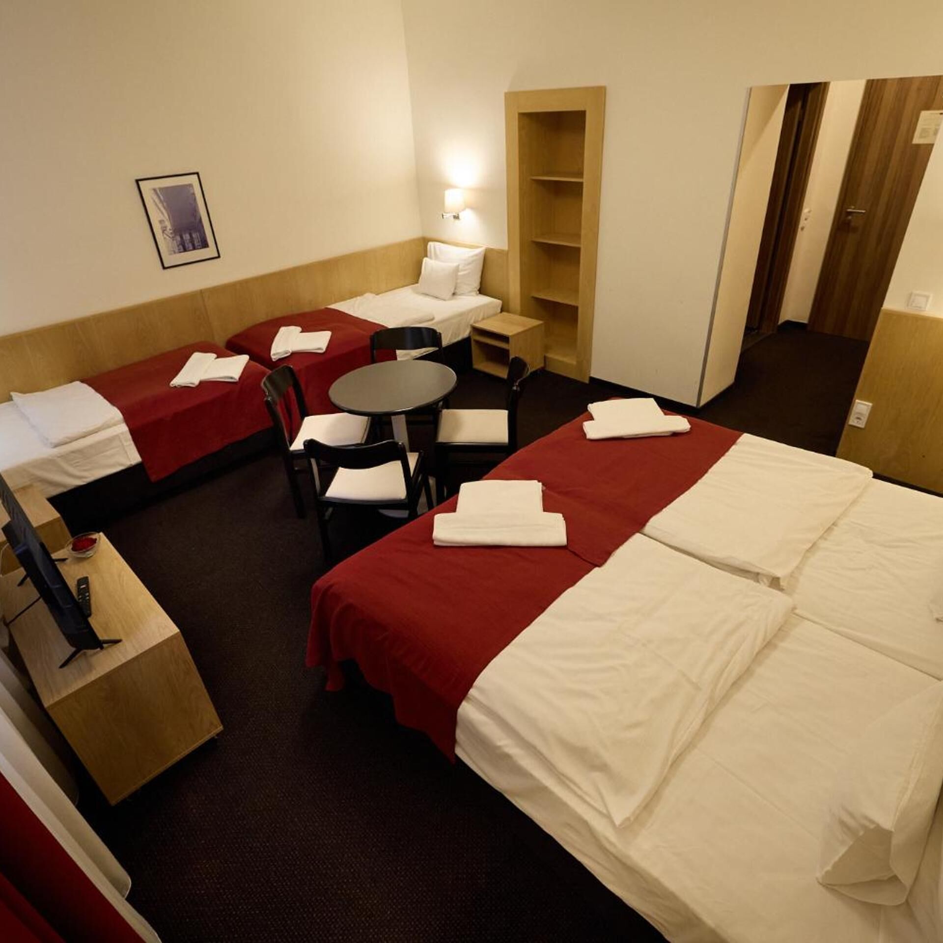 A hotel room with two beds, a small table, chairs, a TV, and a bookshelf.