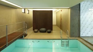 A modern indoor pool with a clear water surface, a wooden deck on one side, and a stone wall with three large stones in the background. - Laterum Conference And Wellness (Pecs)