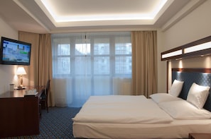 A hotel room with a bed, a desk with a lamp, a television, and a large window with curtains. - Centrum Hotel Debrecen (Debrecen)