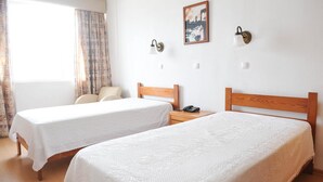 A hotel room with two single beds, a bedside table with a lamp, a painting on the wall, and a window with curtains. - Residencial Sao Francisco (Horta)