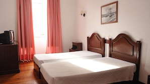 A hotel room with two single beds, a wooden dresser, a nightstand, a lamp, and a framed picture on the wall. - Residencial Sao Francisco (Horta)