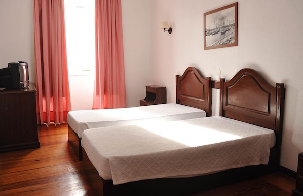 Una camera d'albergo con due letti singoli, una cassettiera in legno, un comodino, una lampada e un quadro appeso al muro.
