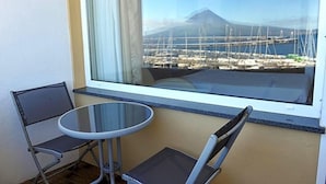 A balcony with a table and chairs, a window with a view of a marina and a mountain. - Residencial Sao Francisco (Horta)