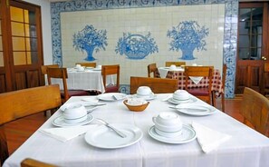 En matplats med bord som är dukade och redo för servering, stolar och en vägg täckt med kakel med blått blommönster.