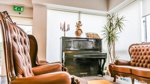 A room with a piano, leather armchairs, a large plant, and a fireplace. - Columbano Hotel Residencial (Peso da Régua)