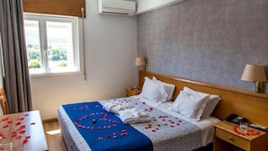 A hotel room with a bed, bedside tables, a window, and an air conditioning unit. - Columbano Hotel Residencial (Peso da Régua)