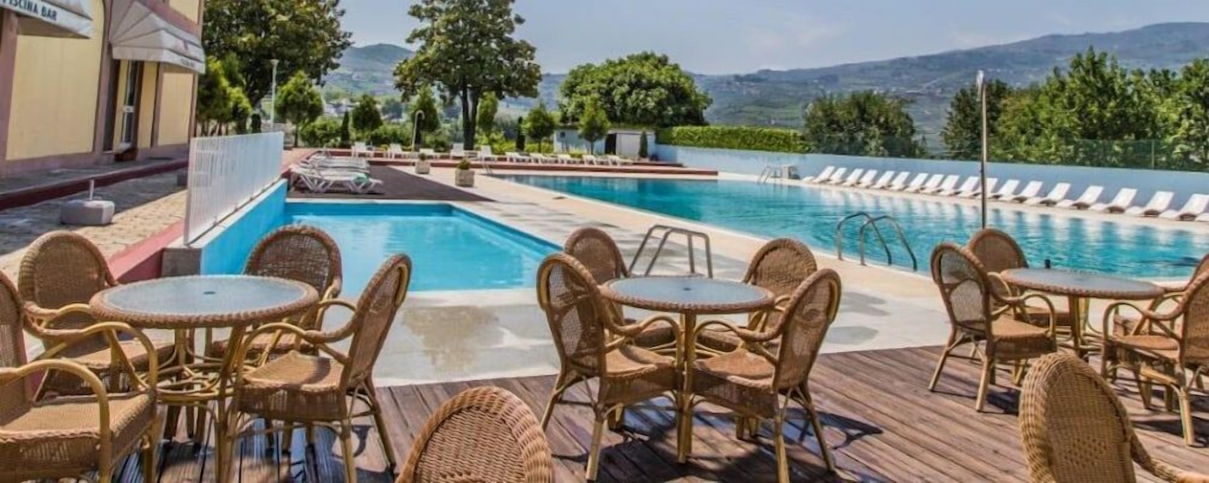 Un espace piscine agrémenté de chaises longues et de tables, entouré de verdure et offrant une vue sur des collines lointaines.