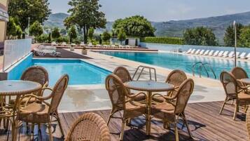 Un espace piscine agrémenté de chaises longues et de tables, entouré de verdure et offrant une vue sur des collines lointaines.