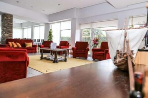 Ein geräumiges Wohnzimmer mit roten Sofas, einem Holztisch und einem Modellschiff.
