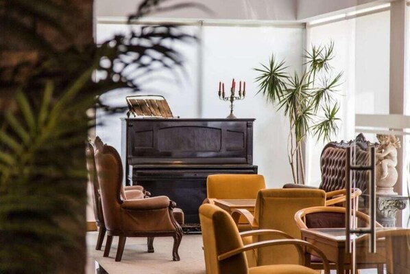 Uma sala de estar com um piano, poltronas de couro e uma mesa de centro de vidro.