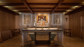An altar with candles, a framed painting, and a cross on the wall. - Crisol Tres Pastorinhos (Ourem)