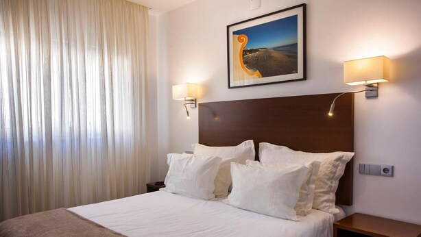 A hotel room with a large bed, two bedside lamps, a nightstand, and a painting on the wall. - Residencial Miramar (Marinha Grande)