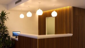 A reception desk with a wooden panel design, a large mirror, and three pendant lights. - Residencial Miramar (Marinha Grande)