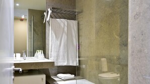 Une salle de bain moderne avec une douche en verre, une baignoire blanche et un mur recouvert de carreaux de marbre.
