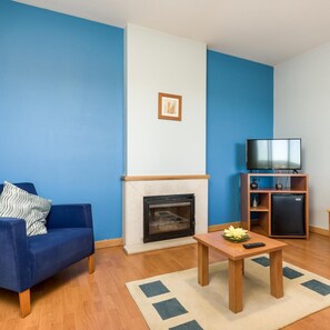A living room with a blue sofa, a fireplace, a television on a stand, and a small refrigerator. - Hotel Do Parque (Sao Pedro do Sul)
