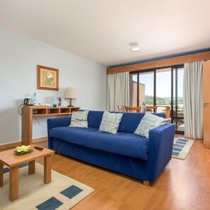 A living room with a blue sofa, wooden coffee table, and a small desk with a lamp. - Hotel Do Parque (Sao Pedro do Sul)