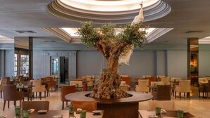 A restaurant with a central tree sculpture, multiple tables, and chairs. - Grande Hotel Lisboa (Sao Pedro do Sul)