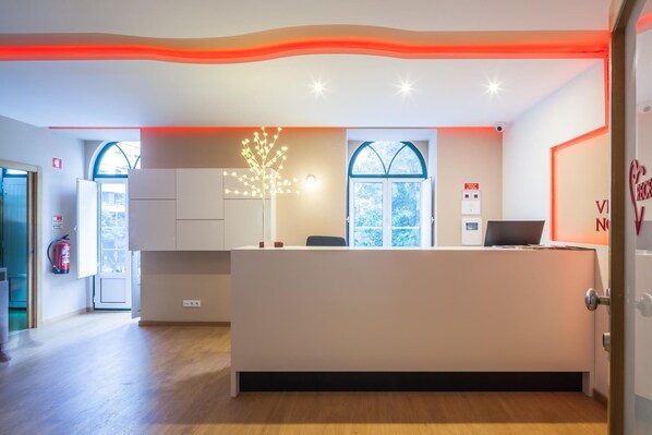 A reception desk with a modern design, a fire extinguisher, and a window with a view of trees. - Residencial Vila Nova (Lisbon)