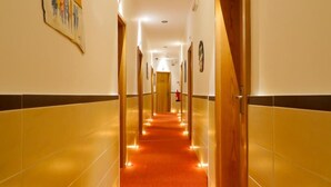 A hotel hallway with a red carpet, wooden doors, and a painting on the wall. - Residencial Vila Nova (Lisbon)