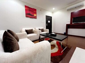 A modern living room with a white sofa set, a black coffee table, and a red abstract painting on the wall. - Raoum Inn Serviced Apartments Hafar Al Batin (Hafr Al Batin)