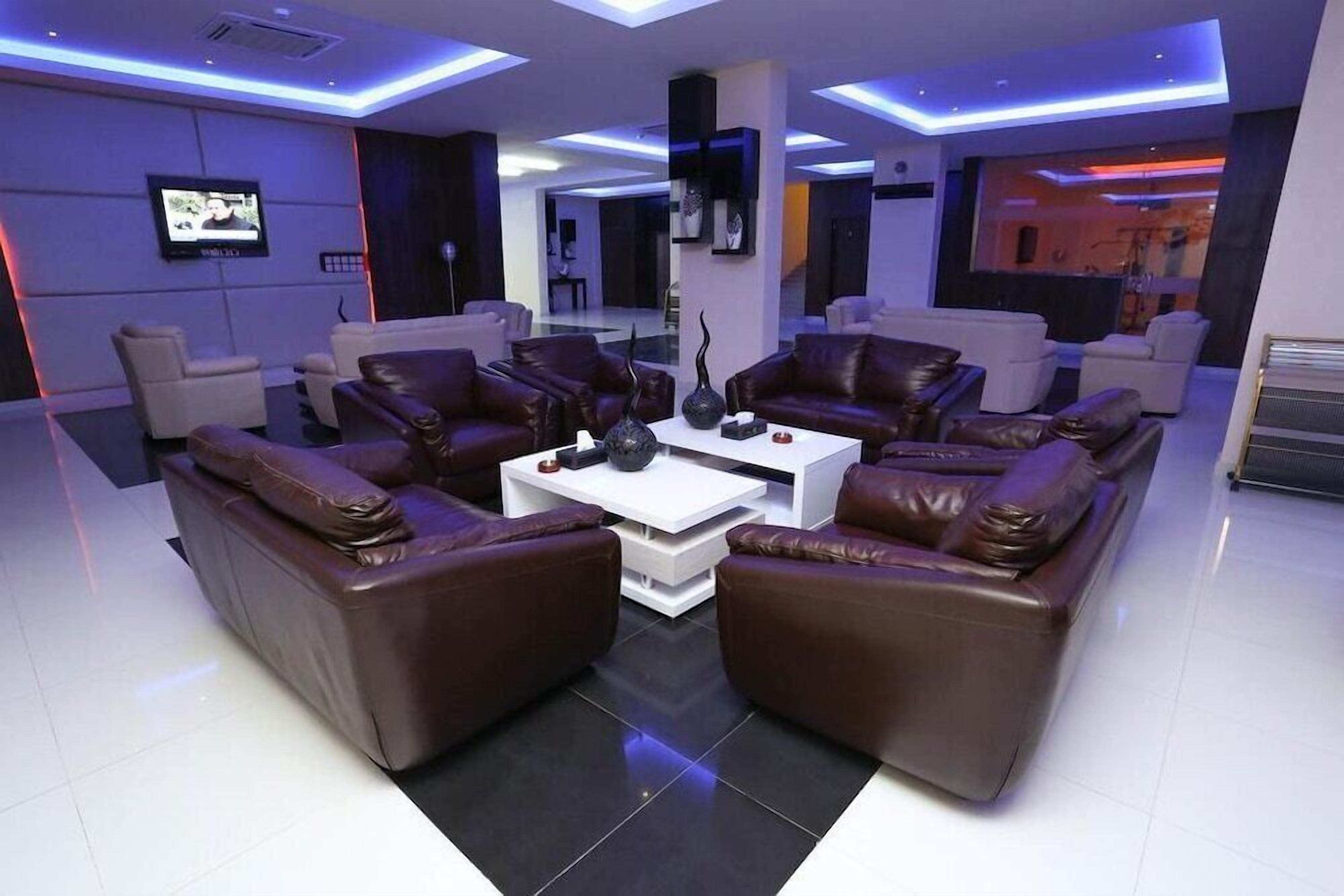 A modern living room with leather sofas, a white coffee table, and a flat-screen TV mounted on the wall.