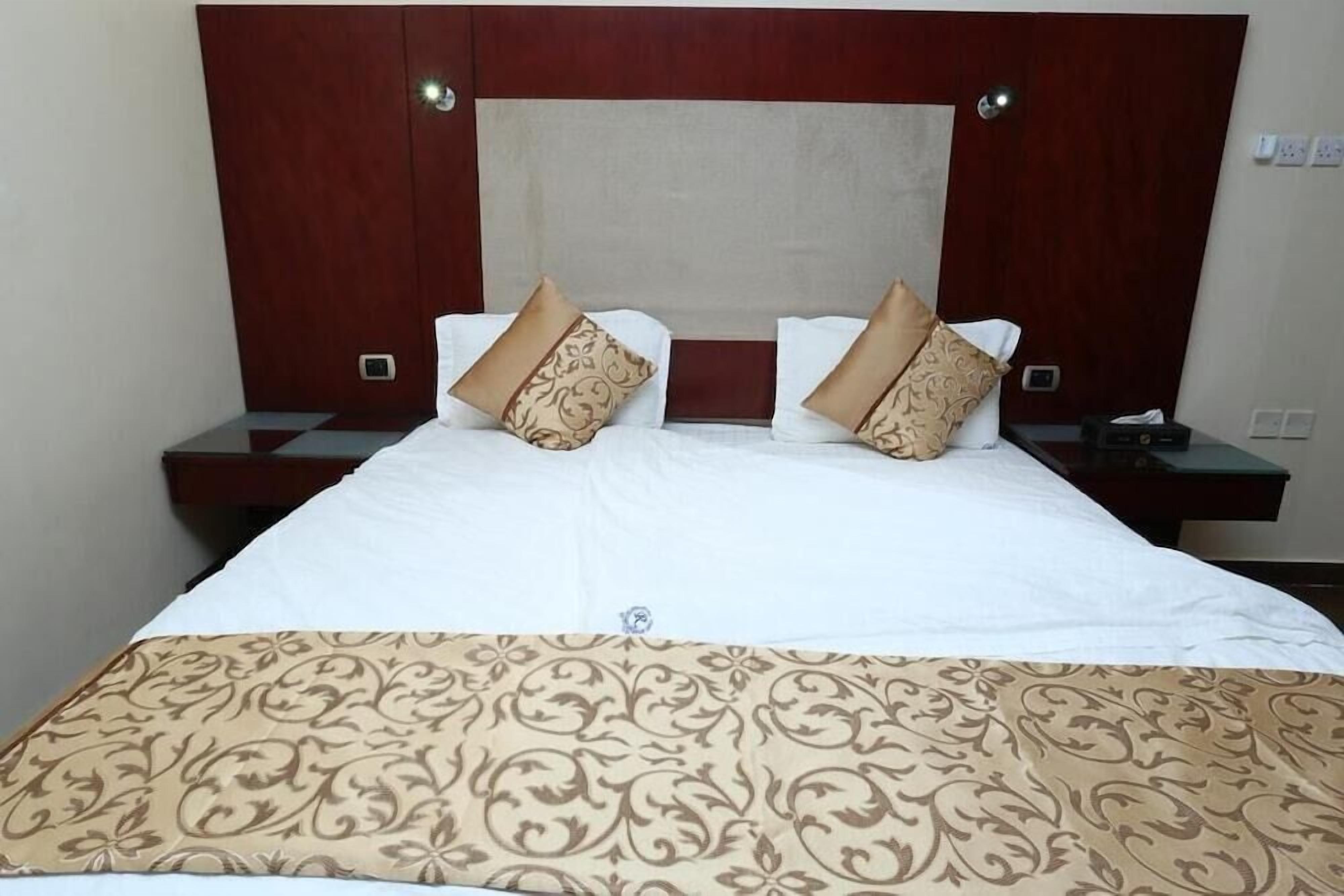 A hotel room with a large bed, two nightstands, a wooden headboard, and a patterned bedspread.