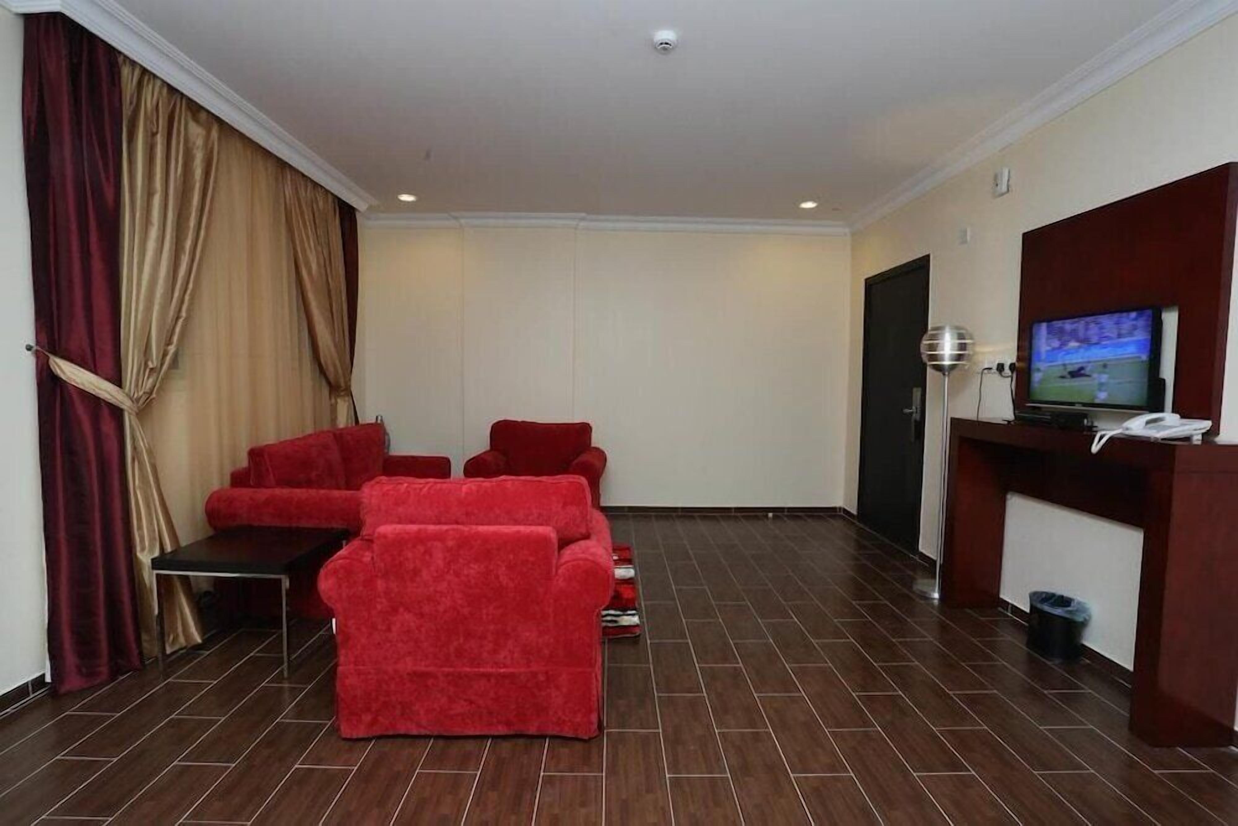 A hotel room with a red sofa set, a small table, a TV, and a reception desk.