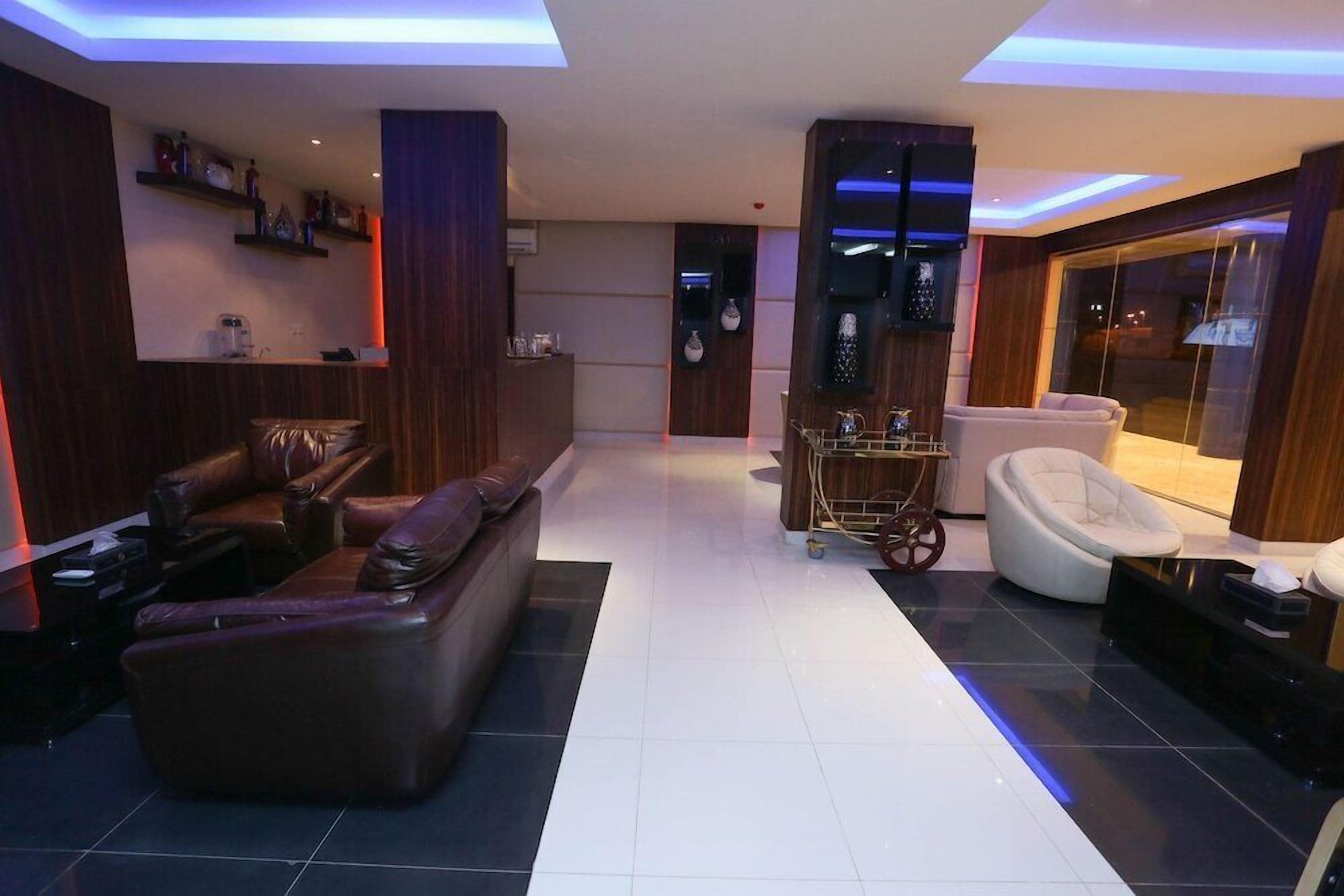A modern living room with a leather sofa, a white chair, a small table, and a TV mounted on the wall.