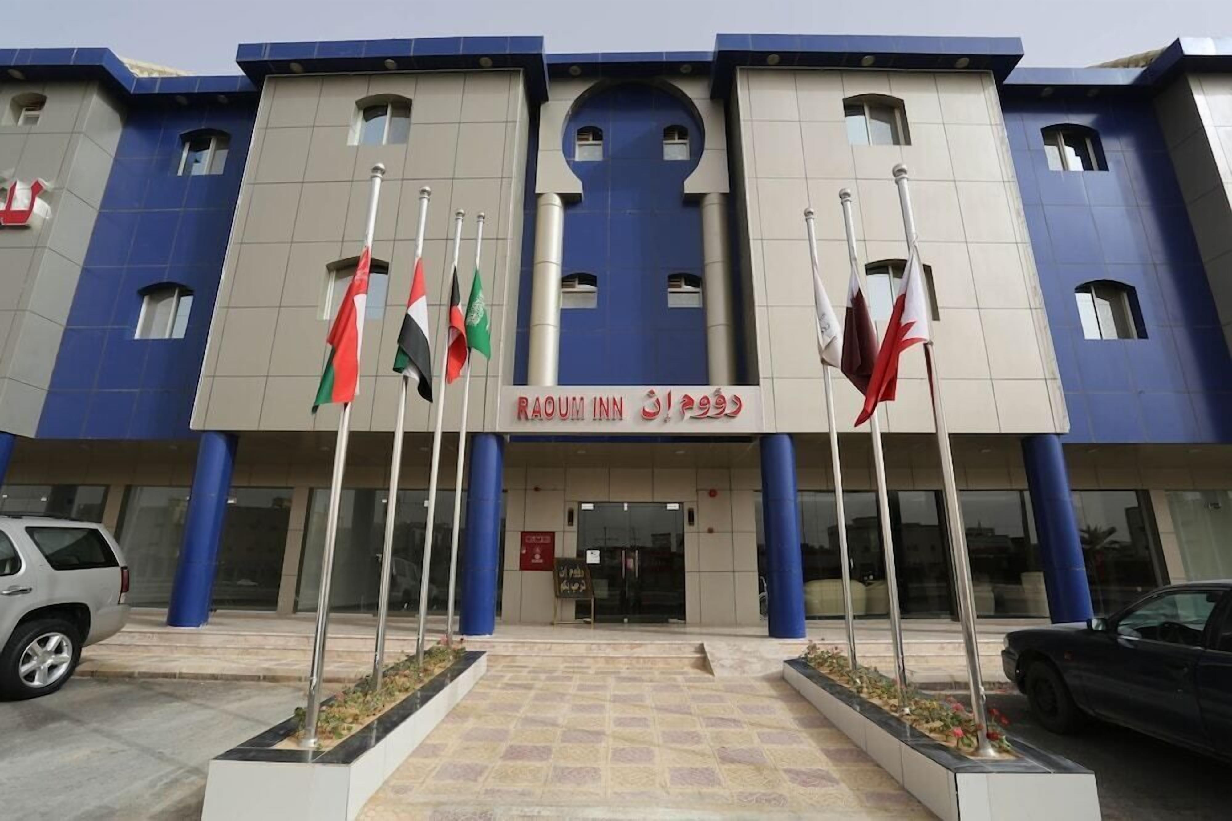 The exterior of a hotel with a modern design, featuring a prominent entrance, multiple flags, and a clear signboard.