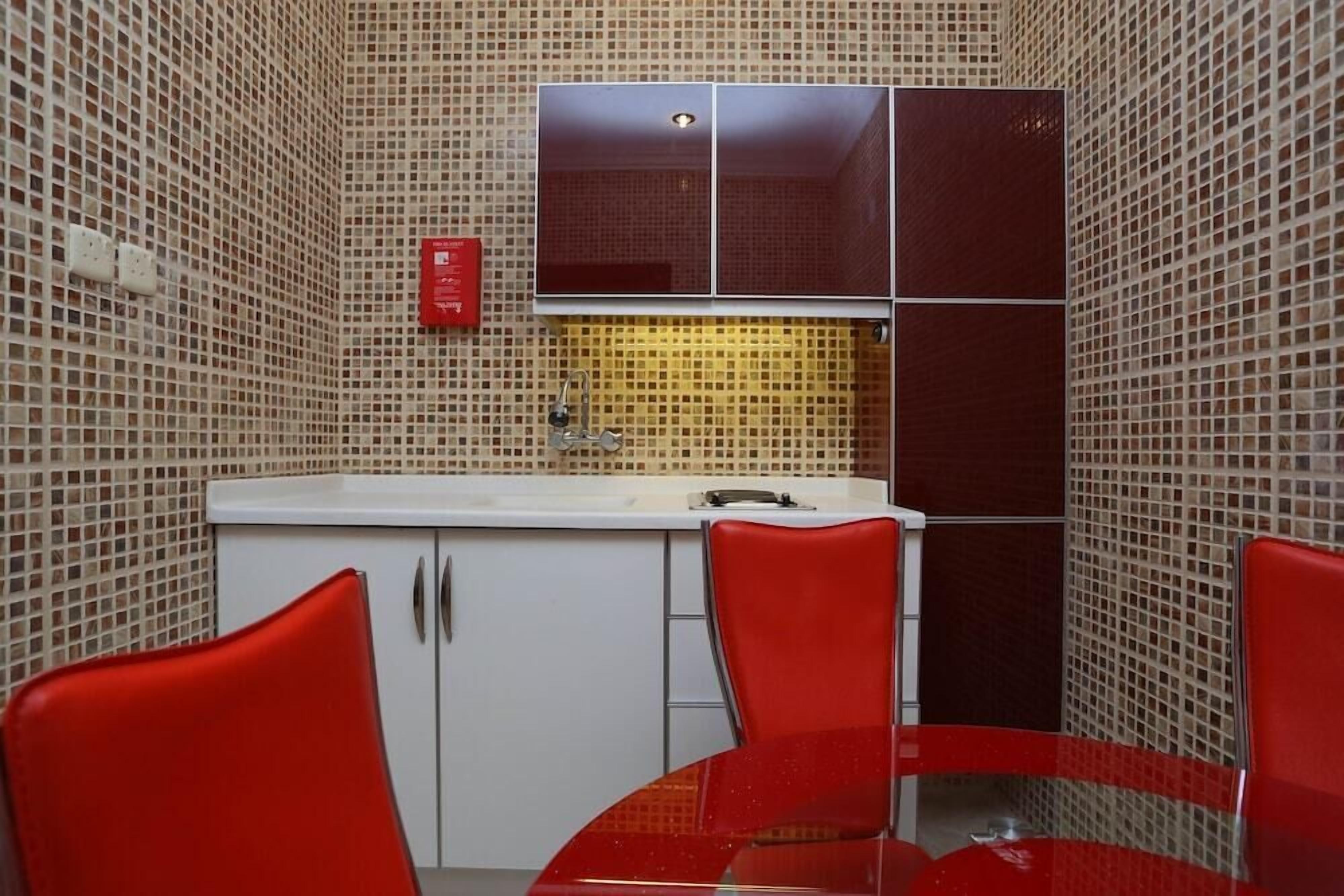 A small kitchen with a white countertop, a sink, and a red cabinet. There are two red chairs around a small table.