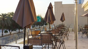 Outdoor seating with umbrellas, a view of palm trees, and a road sign in the background. - Almuhaidb Residence Garnata (Riyadh)