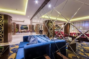 A modern hotel lobby with a blue sofa, red chairs, and a geometric glass partition. - Almuhaidb Residence Garnata (Riyadh)