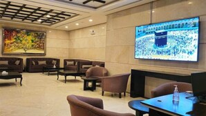 Un hall d’entrée avec des canapés, une table basse, un téléviseur diffusant des images d’une foule et un tableau accroché au mur.