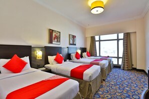 A hotel room with three beds, each with white bedding and red accents, a large window with curtains, and a patterned carpet. - Al Hidayah Towers Hotel (Makkah)