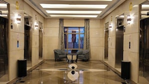 Un hall d’hôtel doté de deux ascenseurs, d’une entrée avec une porte en verre, d’un sol en marbre et d’une table entourée de chaises.